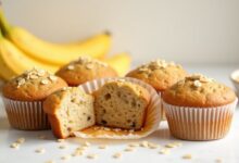 Banana oat muffins topped with rolled oats and sliced bananas on a light baking surface