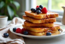 Golden slices of challah bread French toast topped with fresh berries on a white plate